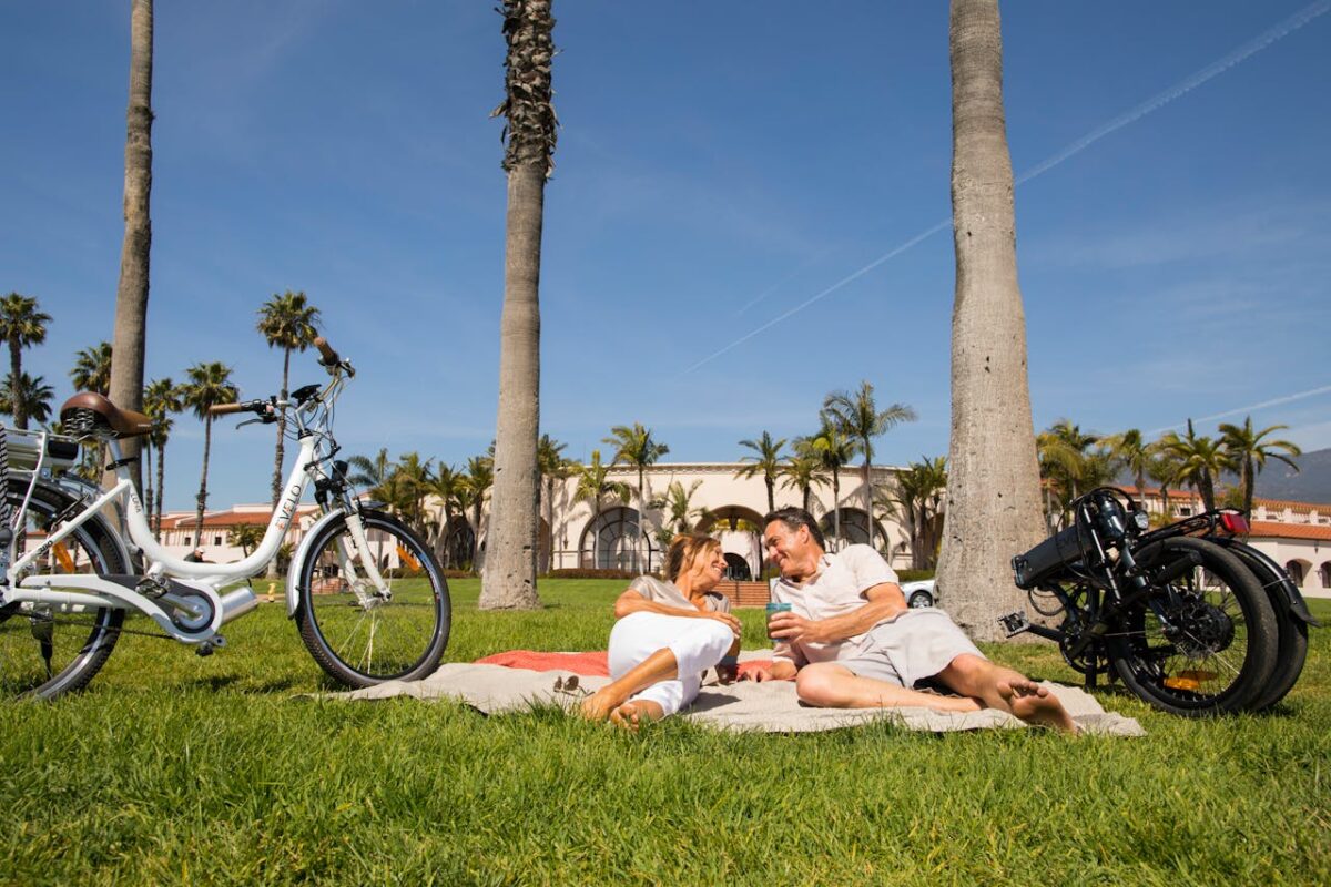 Smiling couple having a picnic under palm trees with bikes nearby on a sunny day.