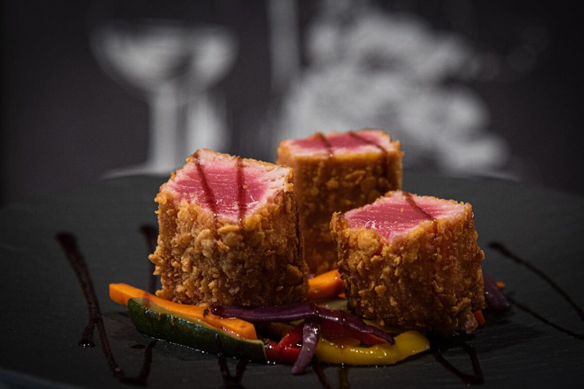 Crispy-coated tuna served with vibrant vegetables on a dark plate.
