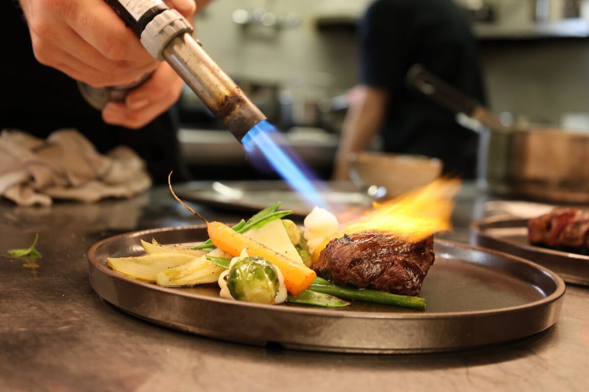 Searing gourmet dish with fresh vegetables using a culinary torch in a professional kitchen.