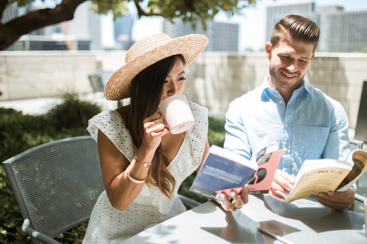 A couple enjoying leisure time outdoors, reading books and sipping coffee in a sunny garden.