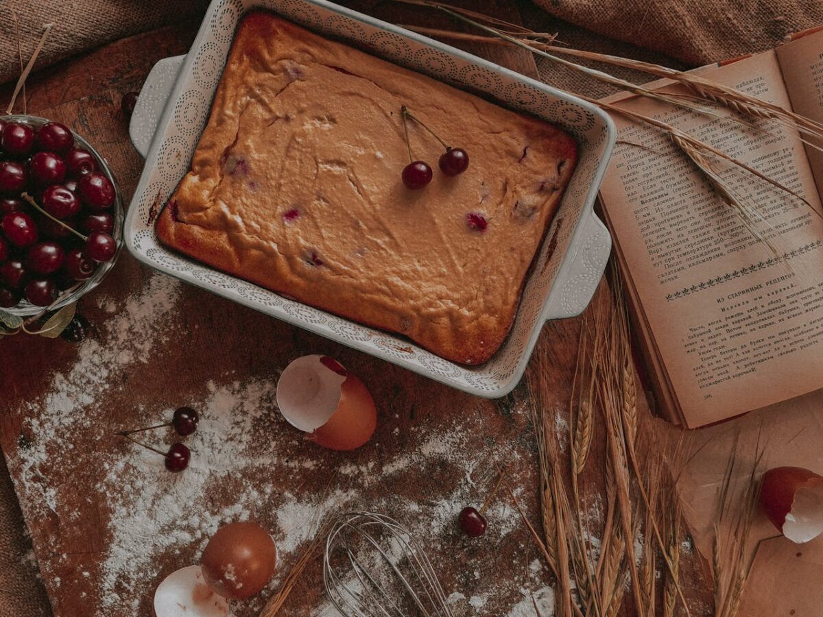 Delicious cherry cake in a rustic setting with eggshells, flour, and open cookbook for baking inspiration.